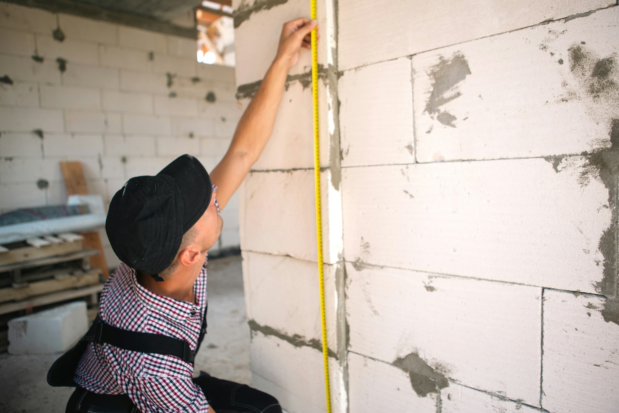 Construction worker at construction site measures the length of window opening and brick wall with t
